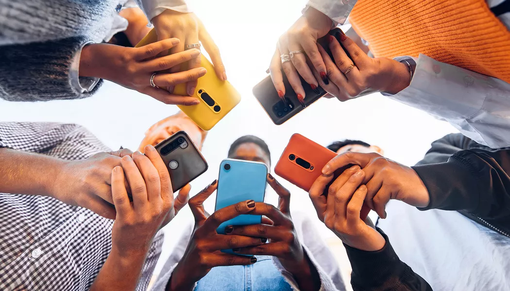 Low-angle view of a group of people standing in a circle, holding colorful smartphones.