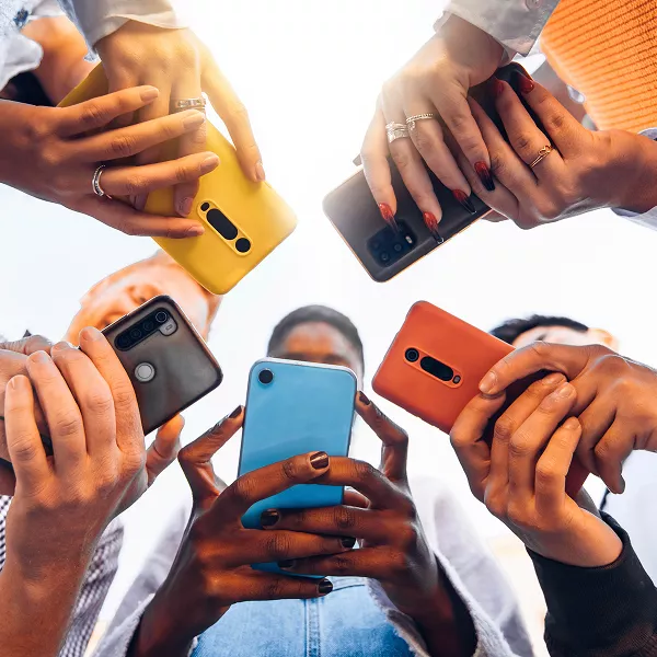 Low-angle view of a group of people standing in a circle, holding colorful smartphones.
