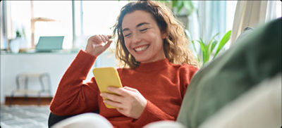 Una mujer sonriente se encuentra sentada en un sofá, mirando su teléfono.