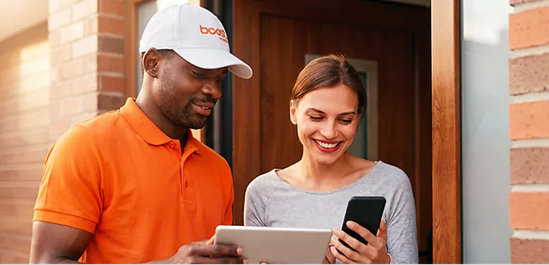 Un repartidor de Boost Mobile ayuda a una clienta sonriente a configurar un nuevo teléfono inteligente en la puerta de su casa.